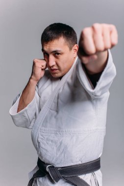 Beyaz arka planda beyaz kimono giyen genç ve güçlü bir adam yumruk atıyor.