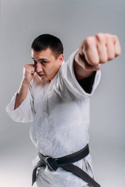 Beyaz arka planda beyaz kimono giyen genç ve güçlü bir adam yumruk atıyor.