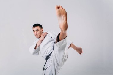 Beyaz arka planda beyaz kimono giyen genç ve güçlü bir adam yumruk atıyor.