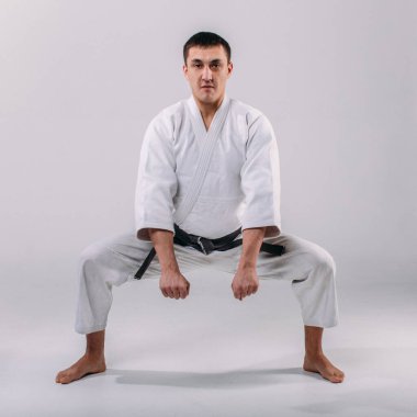 Beyaz arka planda beyaz kimono giyen genç ve güçlü bir adam yumruk atıyor.