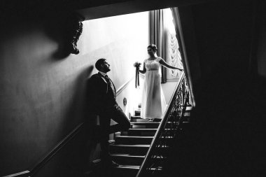 Bir düğün çifti, basamaklarda dikiliyorlar, bir adam duvara yaslanıyor ve kız merdivenlerden iniyor.