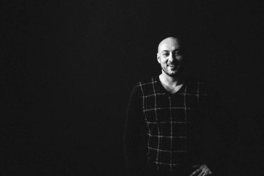 Gözlüklü, koyu renk elbiseli, kel, siyah arka planda genç bir adam elleri ve yüzünde duygular olan bir şey gösterir.