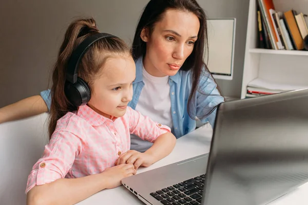 Mom and daughter are at home today. They work remotely on a laptop. Mom helps her daughter complete tasks on a computer.