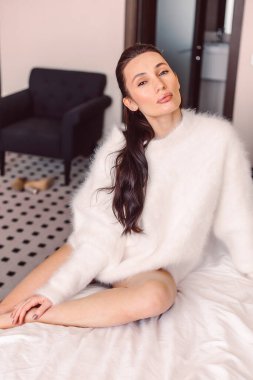 Günaydın, beyaz kazaklı güzel esmer kız ve beyaz keten büyük beyaz bir yatakta oturuyor, güzellik ve şefkat.