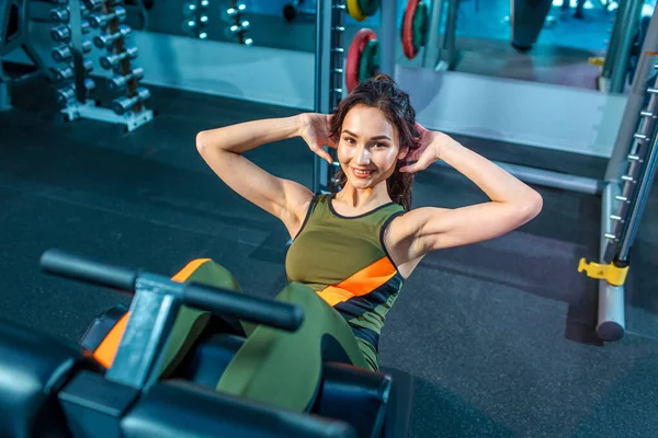 Genç, güzel bir kız, spor figürlü ince bir kız, arka planda aynalar ve fitness ekipmanlarıyla fitness salonunda. Çeşitli egzersizler yapıyor.