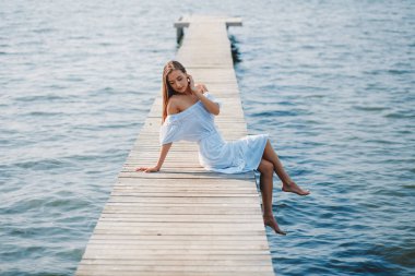 Beyaz bir yaz elbisesi içinde genç bir kız göle gitti. Uzun bir ahşap iskele boyunca. Yaz güneşi parlıyor.