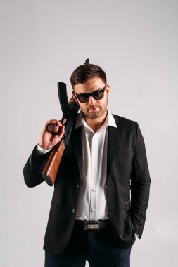 Siyah takım elbiseli, elinde silahla stüdyoda beyaz bir geçmişi olan genç bir adam bir güvenlik görevlisi, koruma ya da ajan tasvir ediyor.