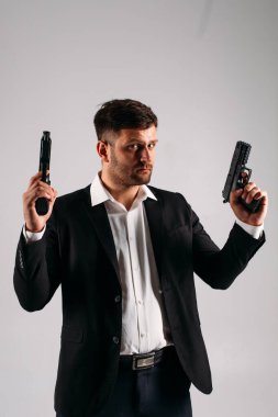 Siyah takım elbiseli, elinde silahla stüdyoda beyaz bir geçmişi olan genç bir adam bir güvenlik görevlisi, koruma ya da ajan tasvir ediyor.