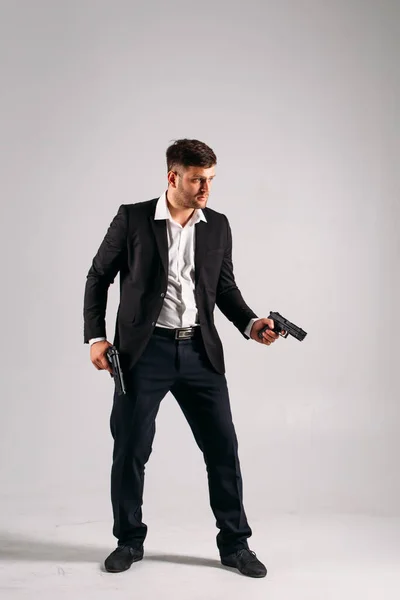 Siyah takım elbiseli, elinde silahla stüdyoda beyaz bir geçmişi olan genç bir adam bir güvenlik görevlisi, koruma ya da ajan tasvir ediyor.