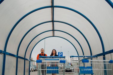 Kırmızı elbiseli genç bir kız ve kırmızı elbiseli bir adam cadde boyunca yürür ve kırmızı ve mavi nesnelerin arka planlarıyla fotoğraf çekerler.