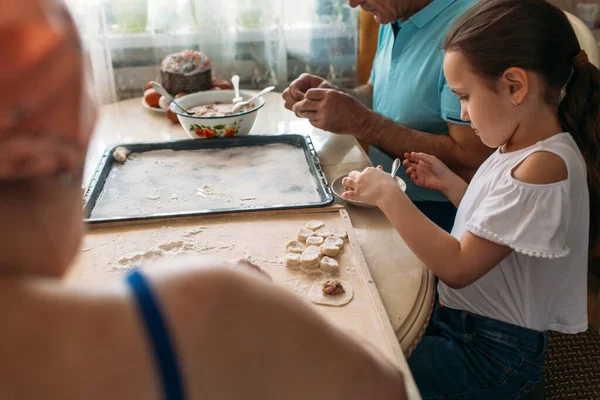 family traditions at the table, granddaughter and mother help grandparents make dumplings, the family is happy together they communicate and enjoy
