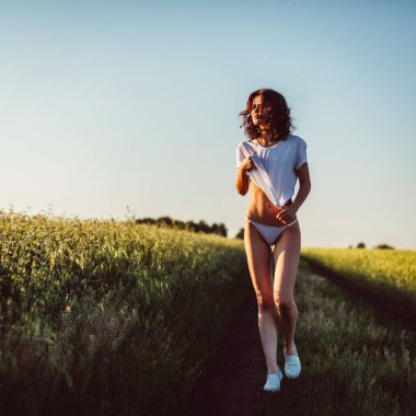 Çicek tarlasında, buğday, güneş, gökyüzü ve yeşillik olan bir tarlada çıplak bir kızın güzel vücudu..