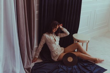 Sade tişörtlü genç, kıvırcık kız bohem tarzında çıplak bir vücutta plağını gramofondan uzatıyor.