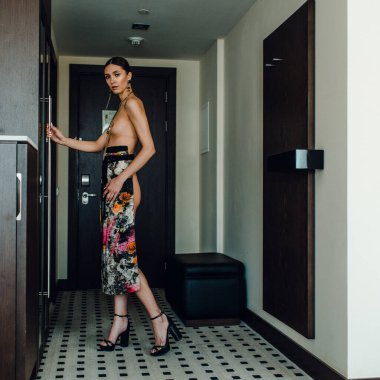 Genç, güzel, uzun boylu, yarı çıplak bir manken soyunma odasında farklı kıyafetler deniyor.