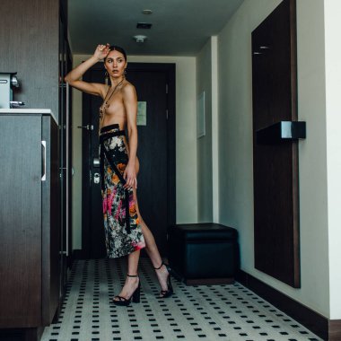 Genç, güzel, uzun boylu, yarı çıplak bir manken soyunma odasında farklı kıyafetler deniyor.