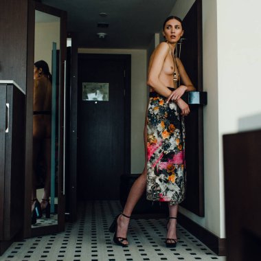 Genç, güzel, uzun boylu, yarı çıplak bir manken soyunma odasında farklı kıyafetler deniyor.