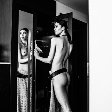 Genç, güzel, uzun boylu, yarı çıplak bir manken soyunma odasında farklı kıyafetler deniyor.