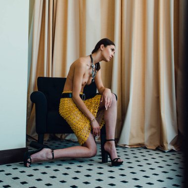 Genç, güzel, uzun boylu, yarı çıplak bir manken soyunma odasında farklı kıyafetler deniyor.