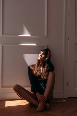 Genç, güzel kız model, uzun boylu, siyah vücutlu, büyük, parlak bir odada, pencereden gelen parlak güneş ışığı üzerine düşüyor.