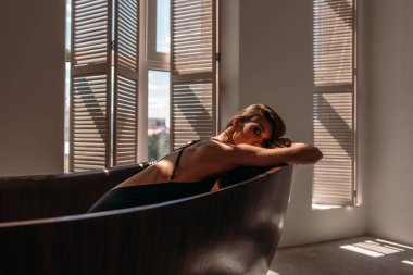 Genç, güzel kız model, uzun boylu, siyah vücutlu, büyük, parlak bir odada, pencereden gelen parlak güneş ışığı üzerine düşüyor.