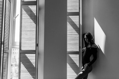 Genç, güzel kız model, uzun boylu, siyah vücutlu, büyük, parlak bir odada, pencereden gelen parlak güneş ışığı üzerine düşüyor.