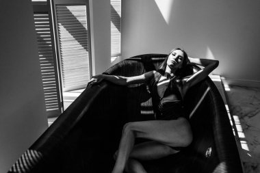 Genç, güzel kız model, uzun boylu, siyah vücutlu, büyük, parlak bir odada, pencereden gelen parlak güneş ışığı üzerine düşüyor.