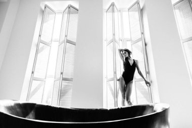 Genç, güzel kız model, uzun boylu, siyah vücutlu, büyük, parlak bir odada, pencereden gelen parlak güneş ışığı üzerine düşüyor.