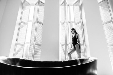 Genç, güzel kız model, uzun boylu, siyah vücutlu, büyük, parlak bir odada, pencereden gelen parlak güneş ışığı üzerine düşüyor.