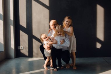 Baba ve çocukları karanlık duvarları olan güneşli bir odada babalarını seviyorlar, onunla oynuyorlar ve sarılıyorlar.