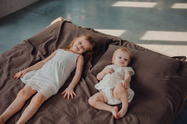 Baba ve çocukları karanlık duvarları olan güneşli bir odada babalarını seviyorlar, onunla oynuyorlar ve sarılıyorlar.