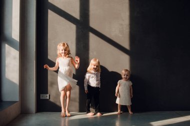 Baba ve çocukları karanlık duvarları olan güneşli bir odada babalarını seviyorlar, onunla oynuyorlar ve sarılıyorlar.