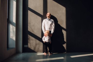 Baba ve çocukları karanlık duvarları olan güneşli bir odada babalarını seviyorlar, onunla oynuyorlar ve sarılıyorlar.