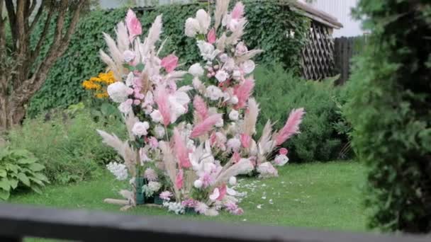 阳光下的一个美丽的拱门 由淡淡的粉色黄草和玫瑰制成 背景是一个小喷泉 从那里流出水 装饰着婚礼 从侧面看 — 图库视频影像