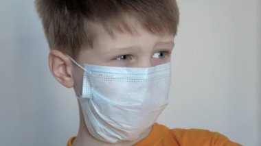 Yüzünde maske olan, beyaz bir arka planda gülümseyen, mesafeye bakıp sevinen mavi gözlü bir çocuğun yakın çekimi.