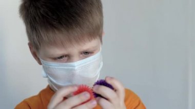 Beyaz arka planda, maske takmış mavi gözlü bir çocuk ellerini Coronavirus 'a benzeyen toplarına çeviriyor ve onu kokluyor, gülümsüyor.