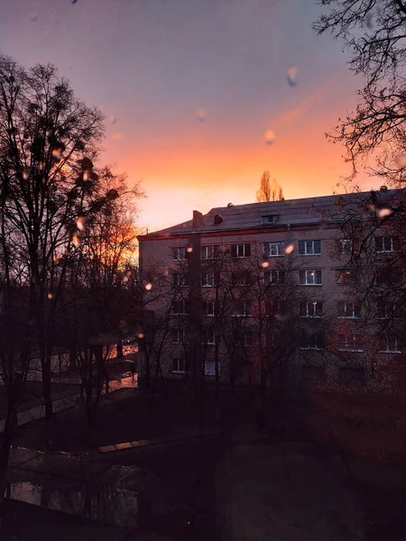 Yağmurdan sonra gün batımı ve penceredeki damlalardan geçen turuncu bir ev. Kharkiv, Ukrayna.