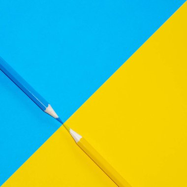 Sarı ve mavi kalemler canlı arka planda birbirlerine bakıyorlar. En Küçük Estetik.