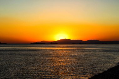 Novorossiysk şehrinin arka planında günbatımı manzaralı vahşi sahil, güneş körfezin arkasına sorunsuzca gitti, deniz kargo gemileri limana gitti.