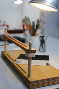 Bir kitap ciltleme ve onarım atölyesindeki ahşap el baskısının arka planda lamba ve farklı aletlerle dikey fotoğrafı