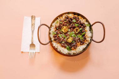 Pirinç ve fasulyeyle süslenmiş bir tavanın havadan görünüşü doğranmış yeşil biberlerle süslenmiş ve yanında çatalla ahşap bir masada servis edilmiş.