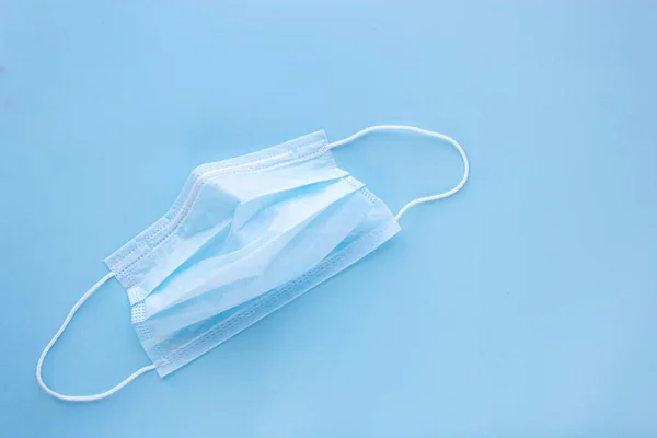 Gebrauchte Medizinmaske mit Gummi-Ohrenbändern auf blauem Hintergrund. Schutz vor Viren und Bakterien — Stockfoto