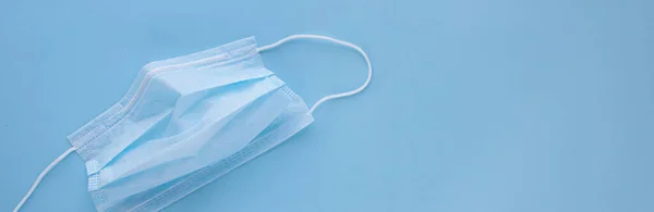  Mavi arka planda lastik kulaklıklı tıbbi maske kullanılmış. Virüs ve bakterilerden koru. Sancak konsepti