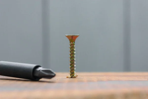 Die Metallschraube, die mit einem Schraubenzieher in die Holzbrettoberfläche eingedrückt wird. Reparaturkonzept zu Hause oder in der Werkstatt — Stockfoto