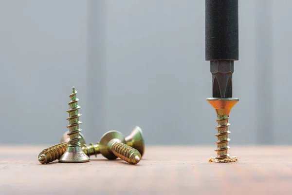 El tornillo de metal tripulado en la superficie del tablero de madera con destornillador. concepto de reparación del hogar o taller —  Fotos de Stock