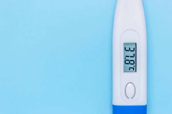 White digital electronic thermometer on a blue background showing high temperature close-up. medical examination concept