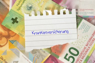 Bir yığın para üzerine sağlık sigortası yazılı not defteri kağıdının yakın plan görüntüsü.