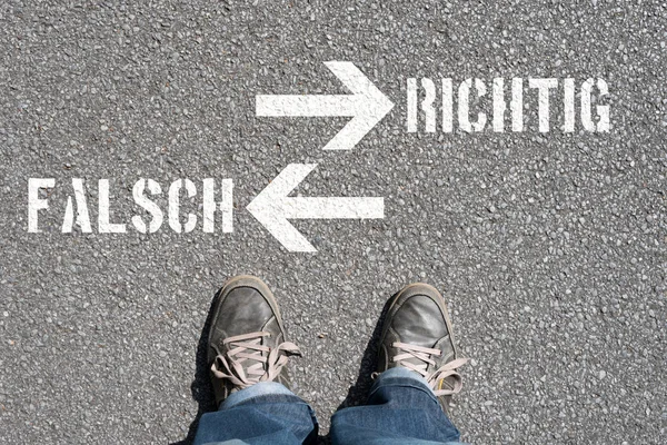 アスファルトの上に立っている人とドイツ語と矢印で偽の碑文と正しい背景 — ストック写真