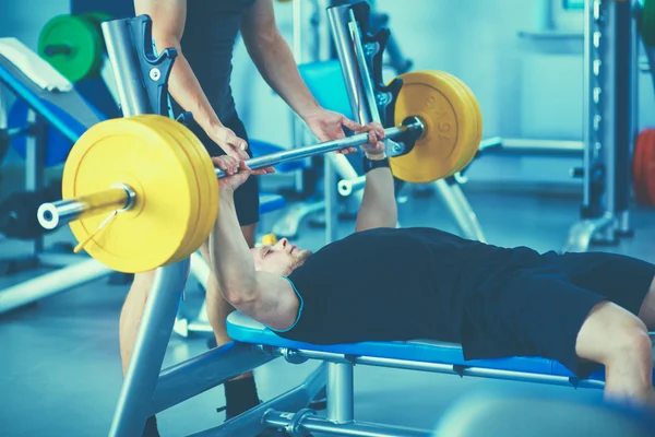 Giovane che solleva il bilanciere in palestra con l'istruttore — Foto Stock