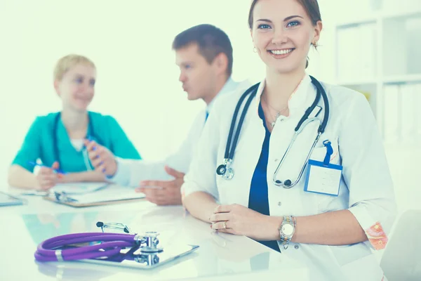 Bonito jovem sorridente médico feminino sentado na mesa — Fotografia de Stock