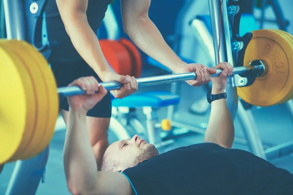 Young man lifting the barbell in gym with instructor — Stock Photo, Image